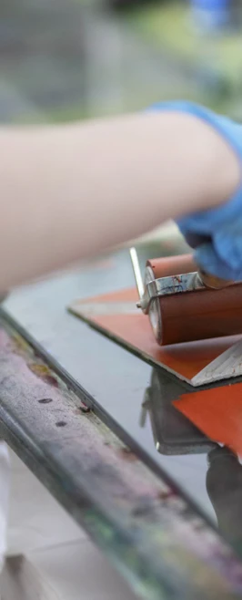 Close-up of a hand in a blue glove rolling ink onto a printmaking plate on a workbench. Close-up of a hand in a blue glove rolling ink onto a printmaking plate on a workbench.